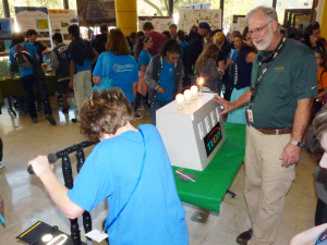 Tampa Electric's Wesley Caldwell, right, helps a young visitor to the Engineering Expo make the connection between motion and power generation - as riders turn the pedals faster, more electricity is generated and the lights light up.
